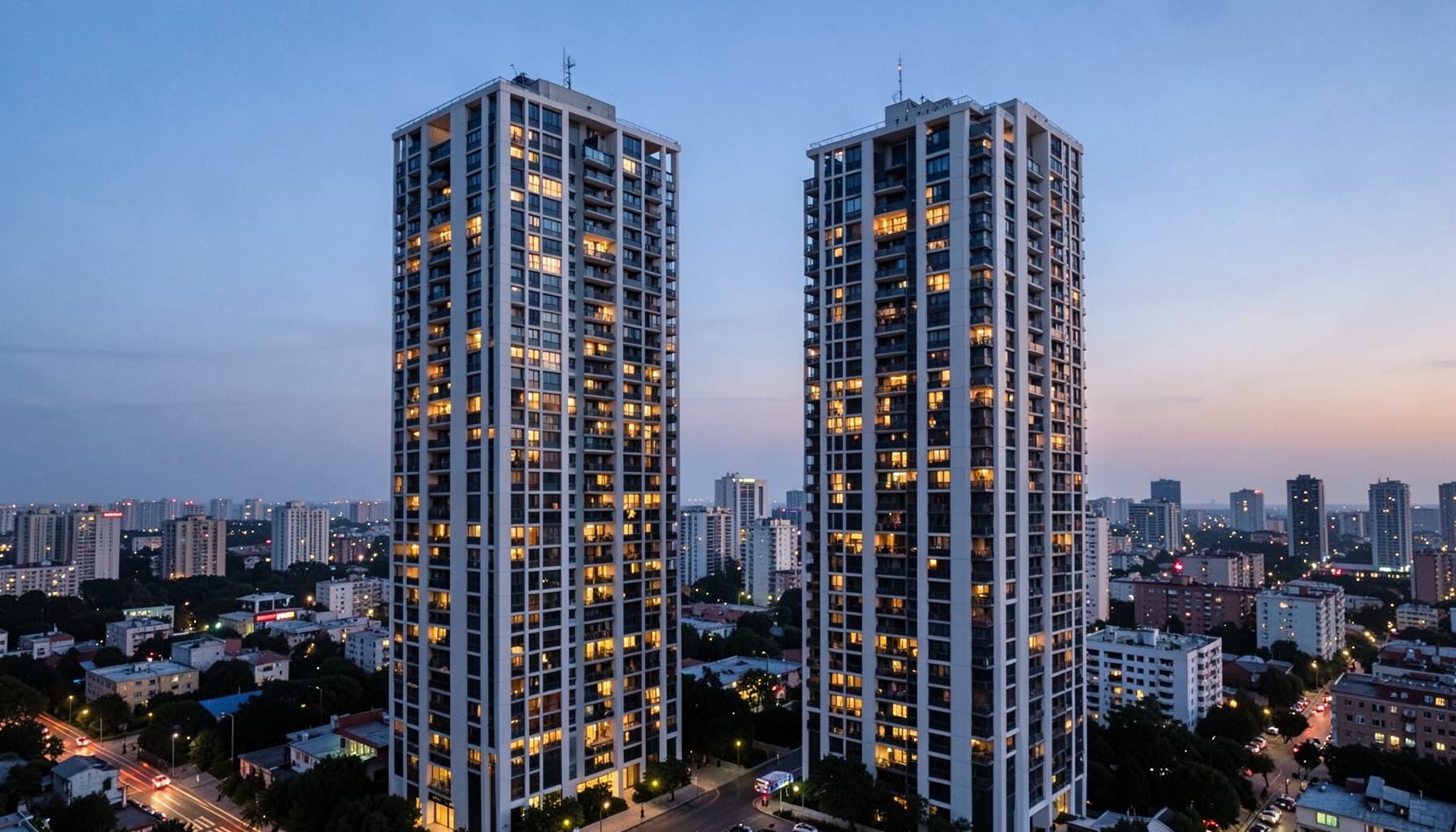 Modern high-rise residential towers at twilight with warm glowing windows, set against a calm urban skyline