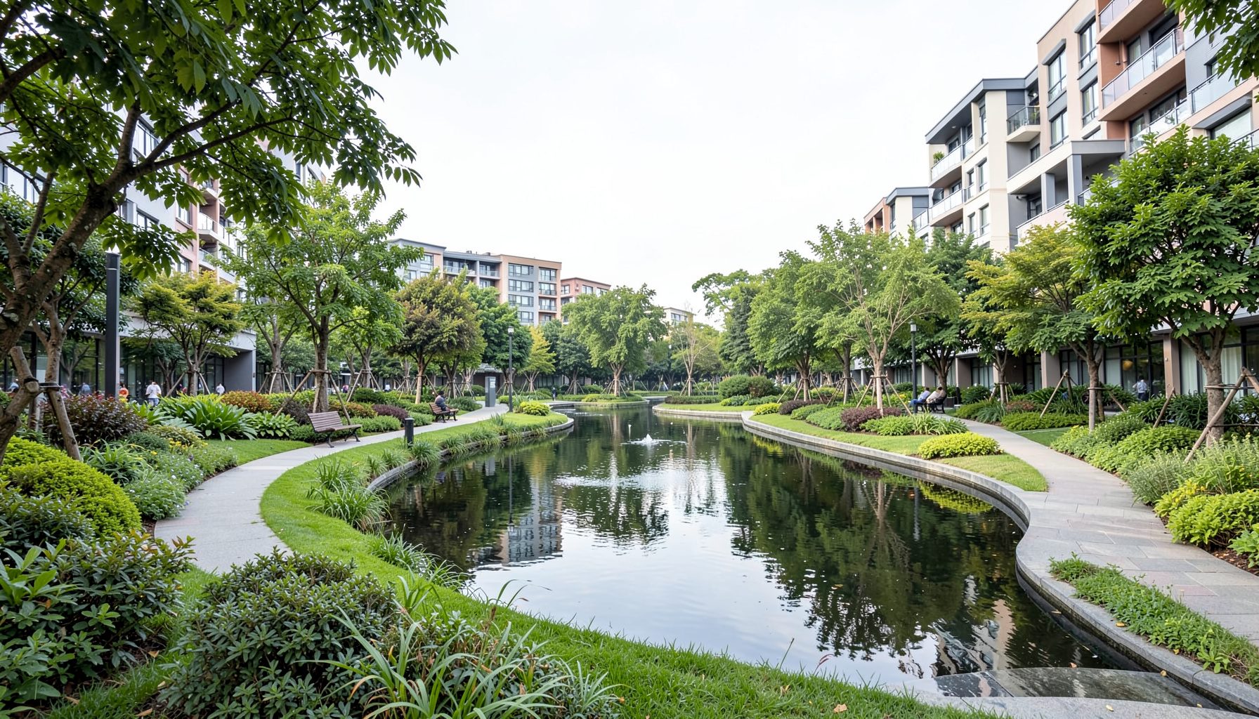Lush landscaped park with reflective water feature and walking paths framed by contemporary residential buildings under soft daylight